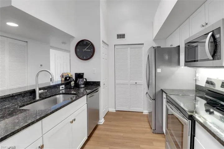 Kitchen featuring sink, white cabinetry, light wood-type flooring, stainless steel appliances, and dark stone counters