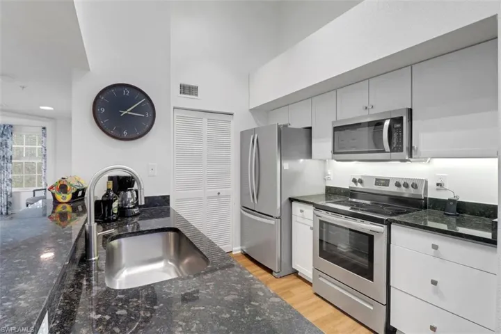 Kitchen featuring white cabinets, appliances with stainless steel finishes, dark stone countertops, sink, and light hardwood / wood-style flooring