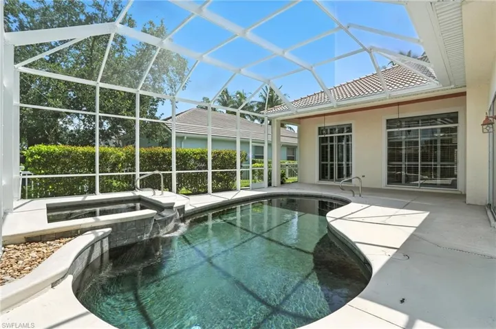 View of swimming pool featuring a patio, a pool with connected hot tub, and glass enclosure - Virtually Edited Image