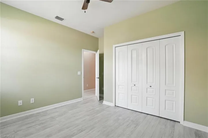 Unfurnished bedroom with light wood finished floors, a closet, and a ceiling fan - Virtually Edited Image