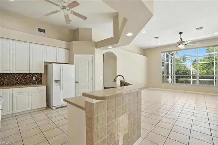 Kitchen with white fridge with ice dispenser, a ceiling fan, light tile patterned flooring, recessed lighting, and decorative backsplash - Virtually Edited Image