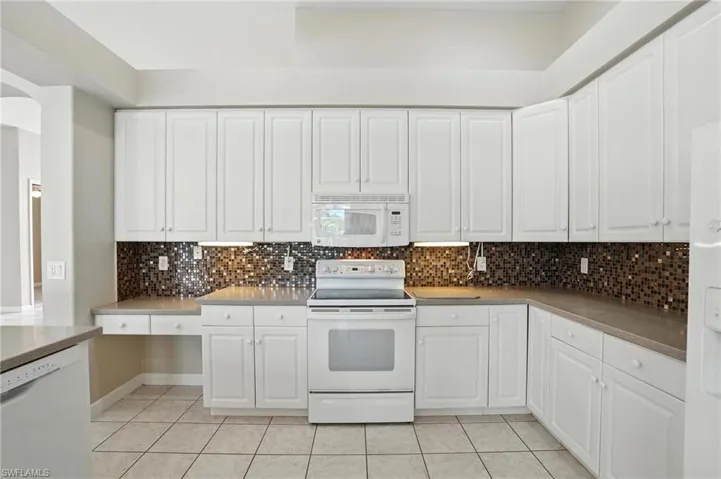 Kitchen with white appliances, light tile patterned floors, arched walkways, tasteful backsplash, and white cabinets - Virtually Edited Image