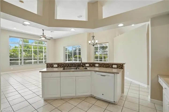 Kitchen with white dishwasher, healthy amount of natural light, a chandelier, white cabinets, and recessed lighting - Virtually Edited Image