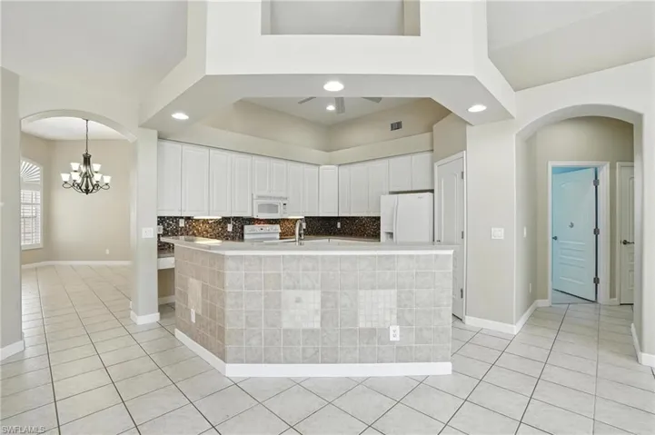 Kitchen with white appliances, arched walkways, light tile patterned flooring, a chandelier, and white cabinets - Virtually Edited Image