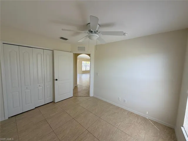 Unfurnished bedroom with arched walkways, a closet, a ceiling fan, and light tile patterned floors