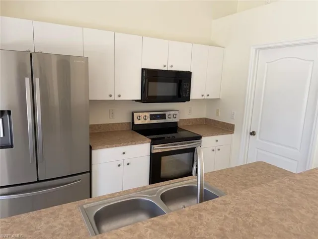 Kitchen featuring stainless steel appliances, white cabinetry, and light countertops