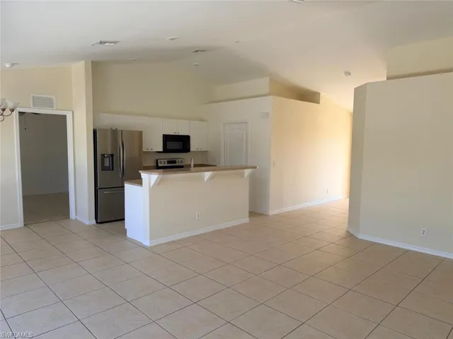 Kitchen with stainless steel appliances, a breakfast bar, white cabinets, vaulted ceiling, and a kitchen island with sink