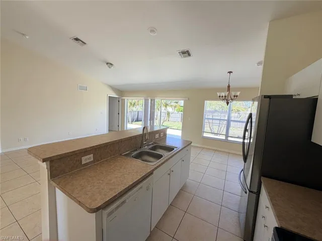 Kitchen with white cabinets, a center island with sink, freestanding refrigerator, hanging lights, and white dishwasher