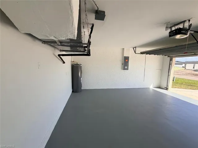 Garage with water heater, electric panel, a garage door opener, and a textured wall