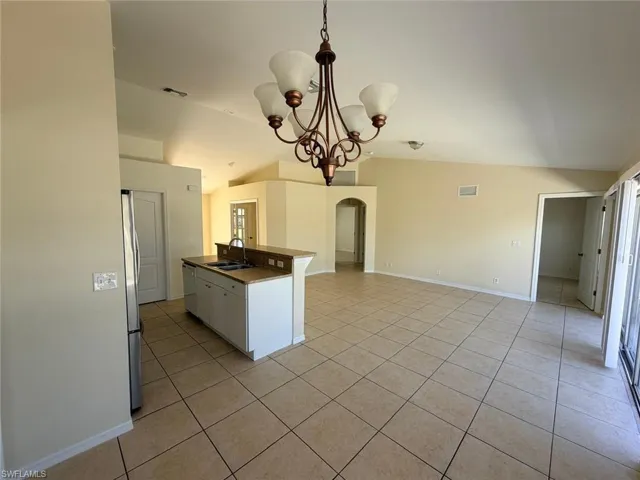 Kitchen featuring arched walkways, vaulted ceiling, hanging lights, light tile patterned floors, and freestanding refrigerator