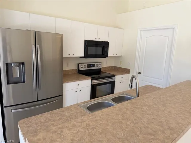 Kitchen featuring stainless steel appliances, white cabinetry, and light countertops