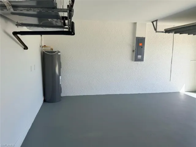 Garage featuring electric panel, water heater, and a textured wall