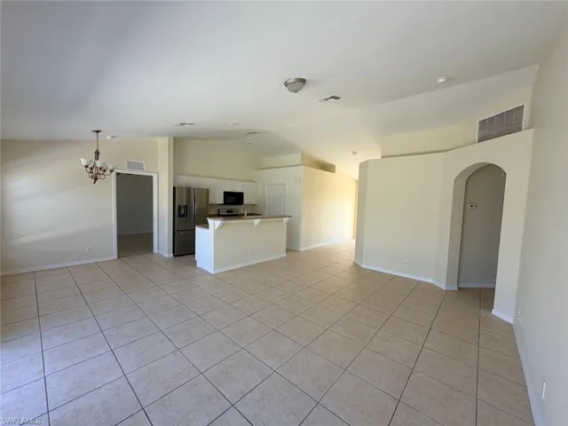 Unfurnished living room featuring lofted ceiling, light tile patterned floors, arched walkways, and suspended lighting