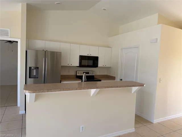 Kitchen with light tile patterned flooring, stainless steel appliances, white cabinets, light countertops, and an island with sink