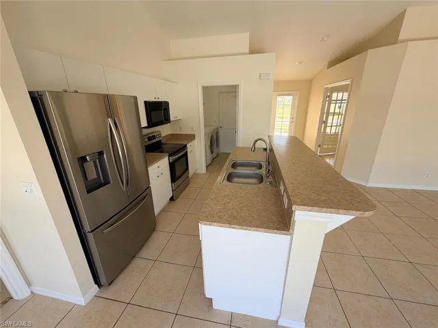 Kitchen with stainless steel appliances, white cabinetry, light tile patterned flooring, separate washer and dryer, and an island with sink