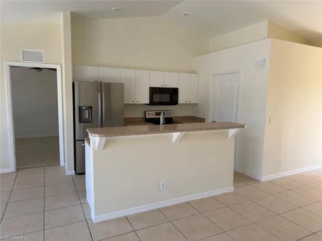 Kitchen with stainless steel appliances, white cabinetry, a kitchen bar, an island with sink, and light countertops