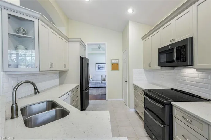 Kitchen with light stone counters, light tile patterned floors, a sink, black appliances, and vaulted ceiling