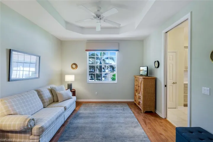 Living area featuring light wood-type flooring, a raised ceiling, baseboards, and a ceiling fan