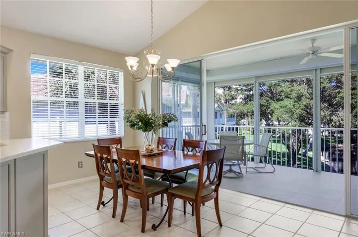 Dining area with light tile patterned flooring, ceiling fan with notable chandelier, baseboards, and vaulted ceiling