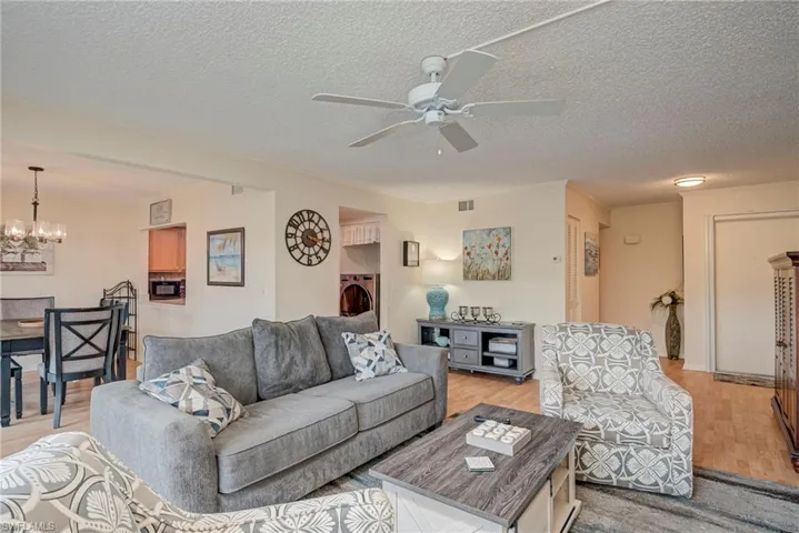 Living area featuring washer / clothes dryer, light wood-type flooring, a textured ceiling, a chandelier, and a ceiling fan