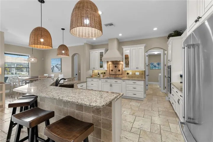 Kitchen featuring arched walkways, stainless steel appliances, pendant lighting, a large island with sink, and glass fronted cabinets