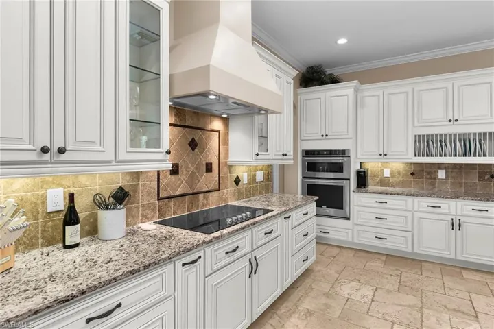 Kitchen with white cabinets, ornamental molding, backsplash, stainless steel double oven, and stone tile flooring
