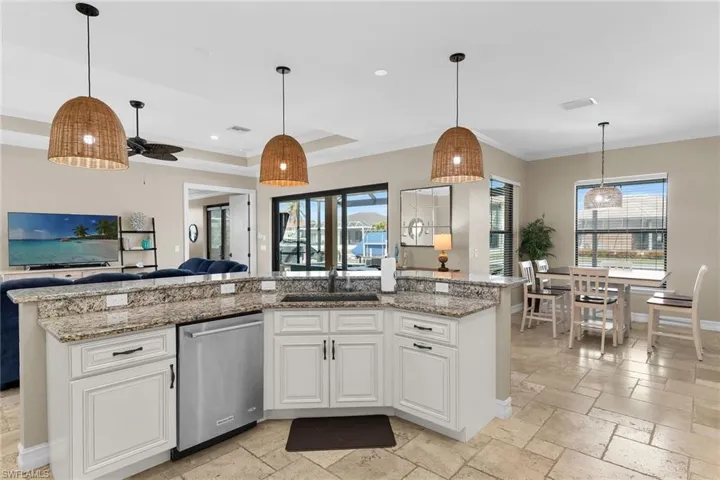 Kitchen with stone tile floors, pendant lighting, white cabinets, stainless steel dishwasher, and light stone countertops