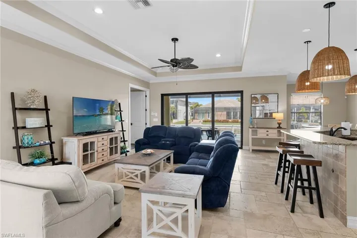 Living area with stone tile floors, a raised ceiling, ornamental molding, ceiling fan, and recessed lighting