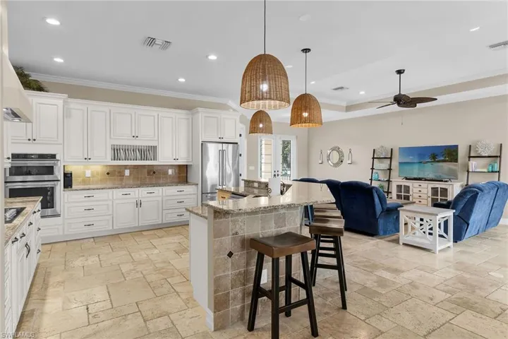 Kitchen featuring crown molding, pendant lighting, a kitchen bar, white cabinetry, and stone tile flooring
