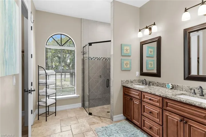 Bathroom with double vanity, a shower stall, and stone tile floors