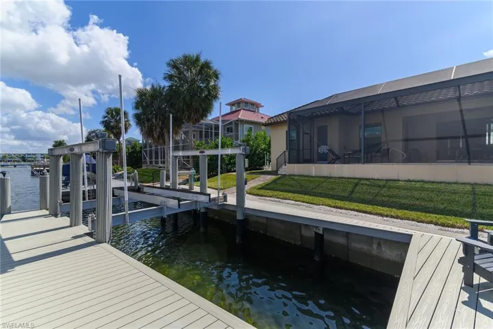 Dock featuring glass enclosure, boat lift, a sunroom, a water view, and a yard