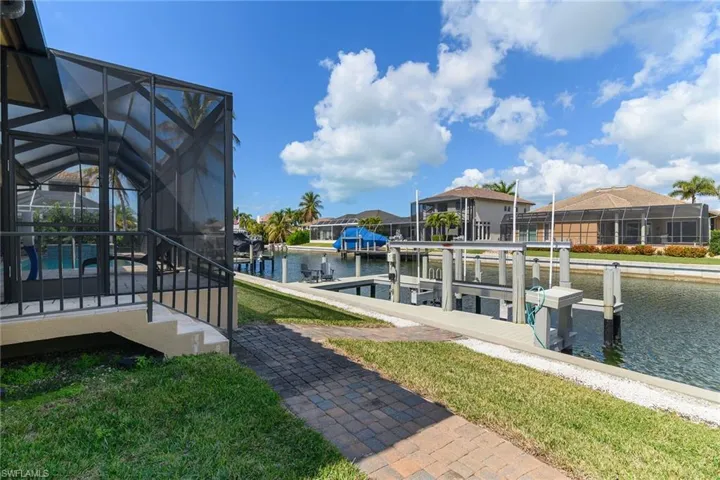 Dock area featuring a sunroom, boat lift, a lanai, a water view, and a yard