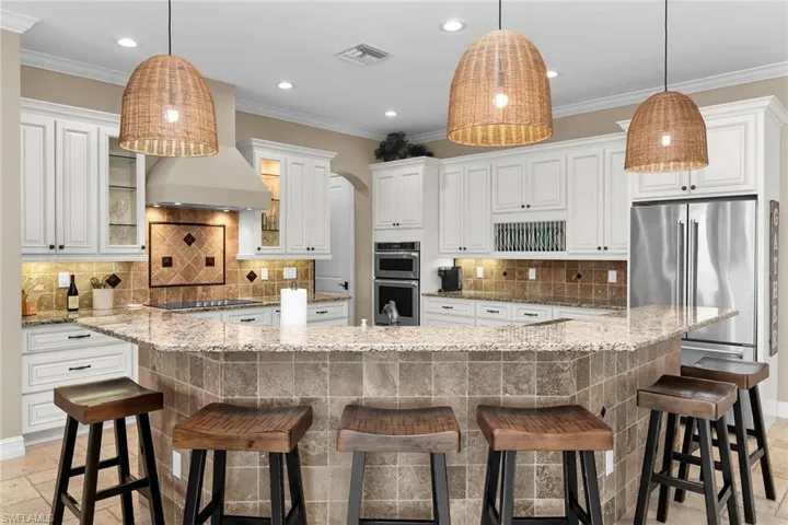 Kitchen with a kitchen bar, stone tile floors, pendant lighting, and crown molding