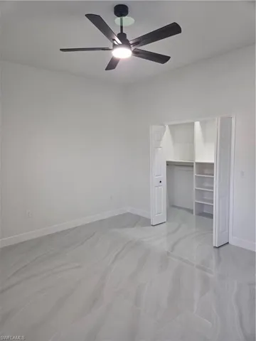 Unfurnished bedroom with ceiling fan and a walk in closet