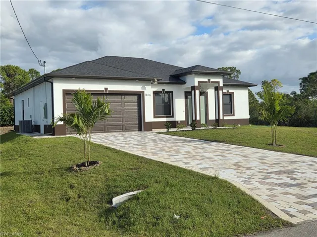 Prairie-style home featuring stucco siding, a front yard, driveway, an attached garage, and roof with shingles