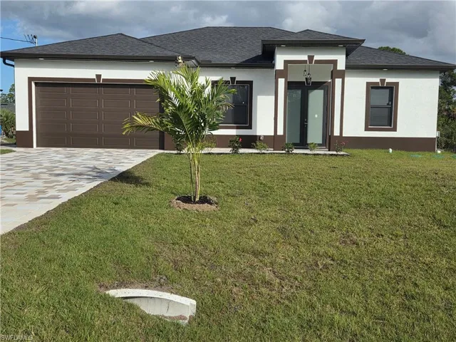Prairie-style house with a front yard, stucco siding, driveway, and roof with shingles