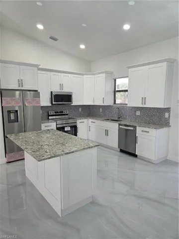Kitchen with light stone counters, white cabinetry, fridge, and recessed lighting