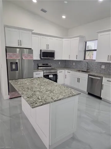 Kitchen with white cabinets, light stone countertops, electric stove, refrigerator, and recessed lighting