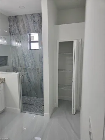 Full bath with a marble finish shower, a walk in closet, and vanity