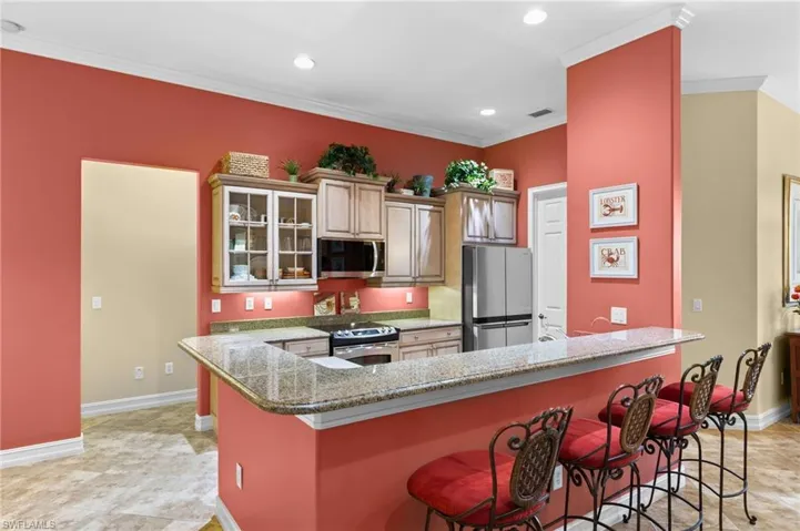 Kitchen featuring appliances with stainless steel finishes, a kitchen breakfast bar, light stone counters, crown molding, and a center island