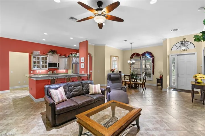 Living room featuring ceiling fan with notable chandelier, light tile patterned floors, and crown molding