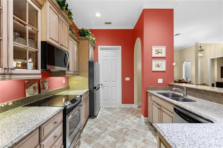 Kitchen with light stone counters, sink, light brown cabinets, appliances with stainless steel finishes, and crown molding