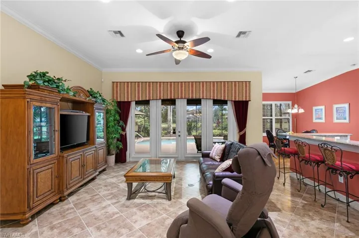 Tiled living room with french doors, ceiling fan with notable chandelier, and ornamental molding