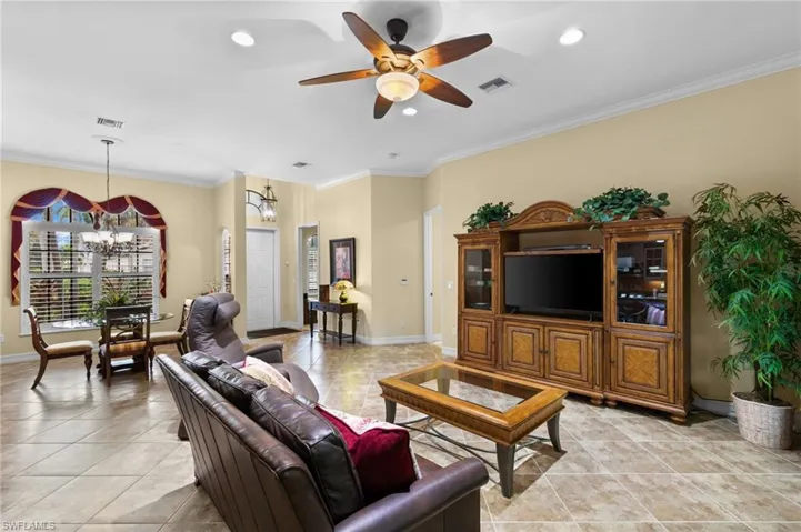 Tiled living room featuring ceiling fan with notable chandelier and crown molding