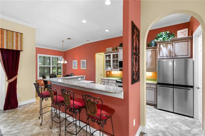 Kitchen featuring a breakfast bar area, a notable chandelier, appliances with stainless steel finishes, decorative light fixtures, and light stone countertops