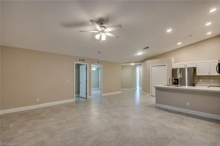 Unfurnished living room featuring ceiling fan, light tile patterned flooring, sink, and lofted ceiling