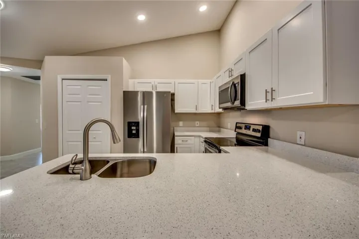 Kitchen featuring light stone countertops, sink, stainless steel appliances, and white cabinetry