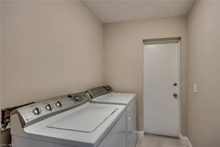 Clothes washing area with washing machine and dryer and light tile patterned floors