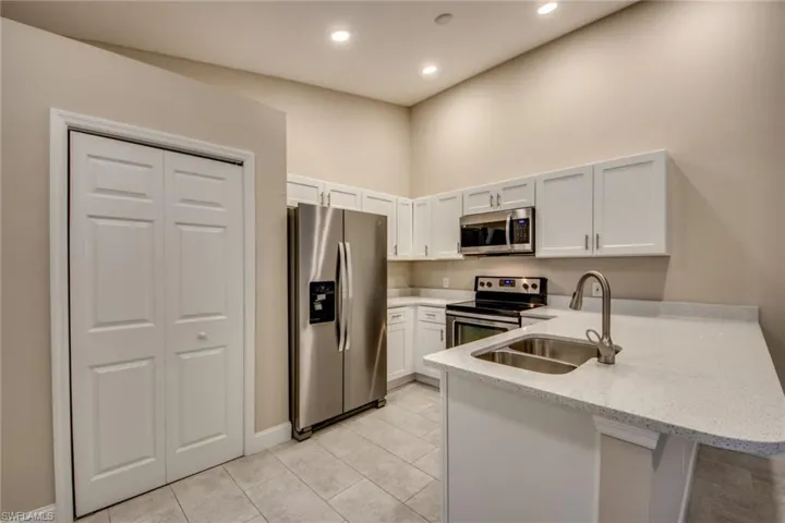 Kitchen with light stone counters, appliances with stainless steel finishes, sink, and white cabinets