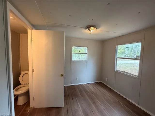 Unfurnished bedroom with dark wood-style floors and a decorative wall